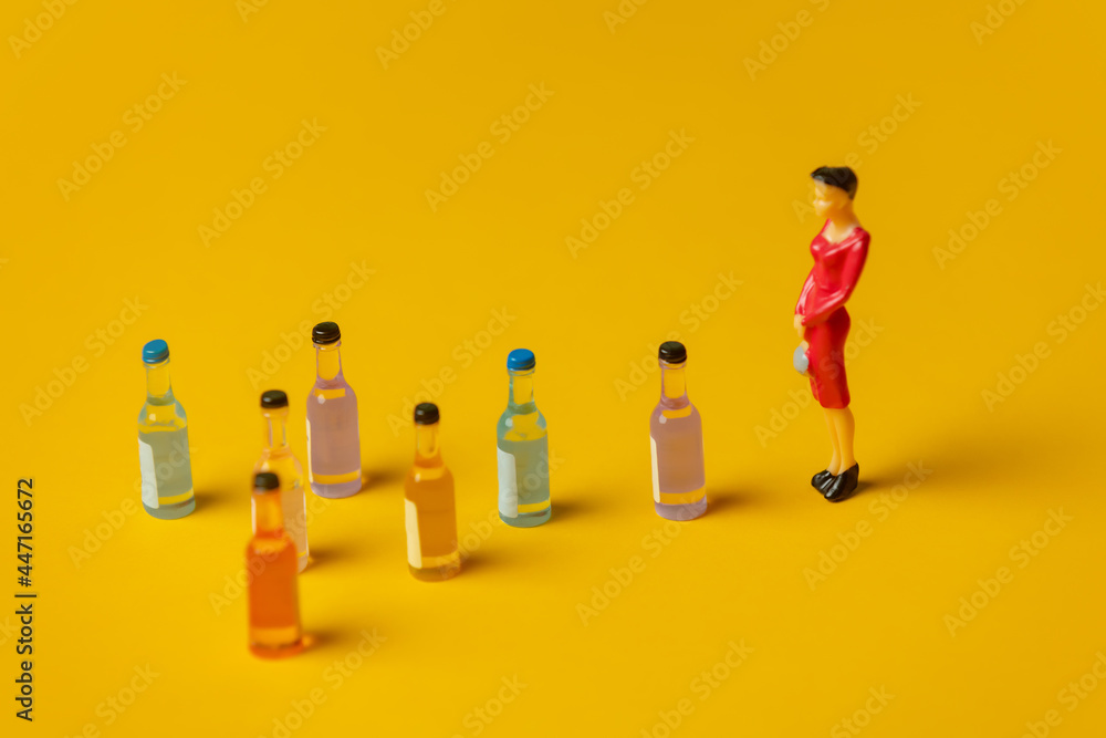  miniature figure of a woman with alcohol bottles in front of her - obrazy, fototapety, plakaty 