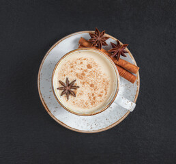 Masala chai tea on a dark background closeup. Traditional Indian hot drink with milk and spices. Top view, flat lay.