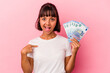 © Asier - Young mixed race woman holding bills isolated on pink background person pointing by hand to a shirt copy space, proud and confident