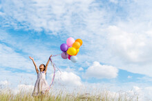 Cheerful Cute Girl Holding Balloons Running On Green Meadow White Cloud And Blue Sky With Happiness. Hands Holding Vibrant Air Balloons Play On Birthday Party Happy Times Summer On Sunlight Outdoor