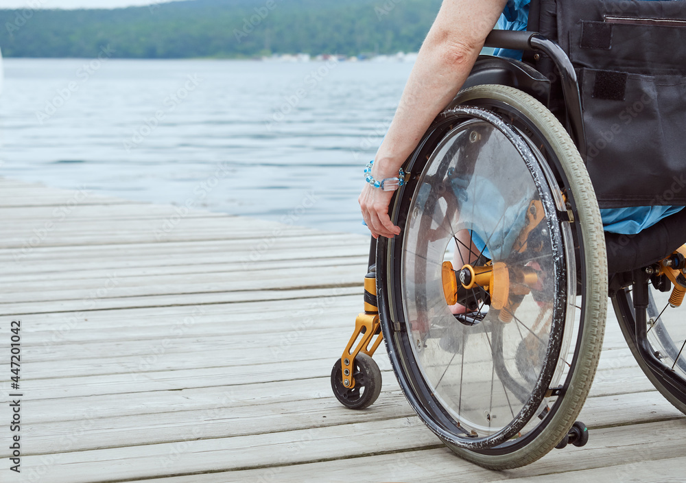 Woman in a wheelchair looking at the sea, part of the image, with copy space - obrazy, fototapety, plakaty 