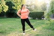 © golubovy - Band exercise. Weight control. Active lifestyle. Body positive. Happy motivated overweight obese woman in sportswear fitness training in sunny green spring park landscape.