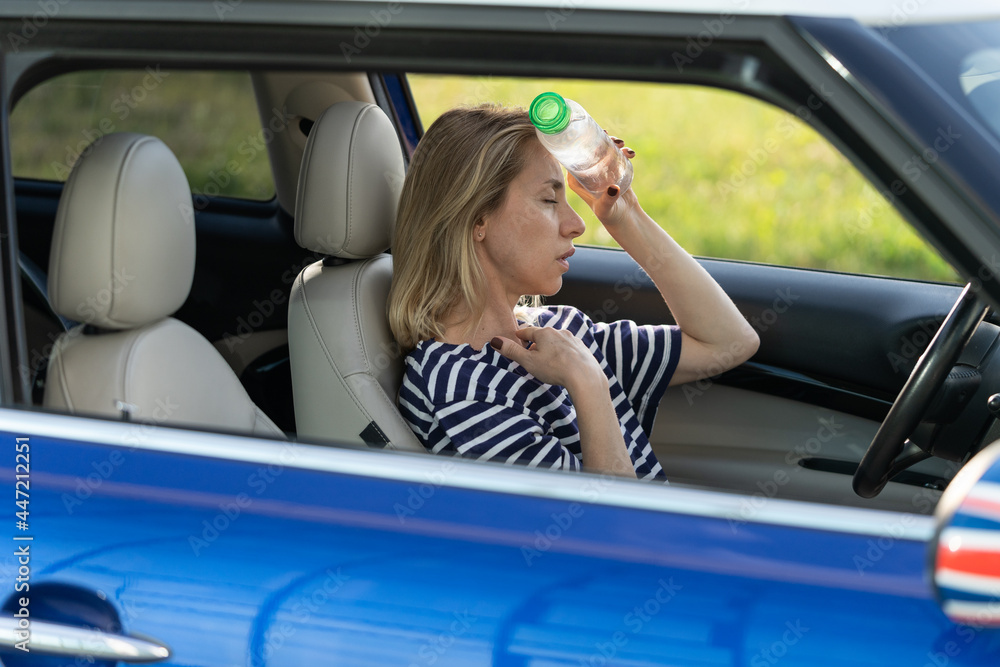 Exhausted woman driver feeling headache, sitting inside her car, applies bottle of water to forehead, hot weather. Tired female stop after driving car in traffic jam. Blood pressure, heat concept.  - obrazy, fototapety, plakaty 