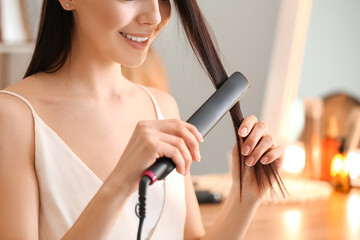 Wall Mural - Beautiful young woman straightening hair at home