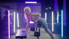 Blonde Girl Lift Hand Bag In The Gym Surrounded By Neon Lights