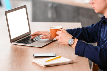 Wall Mural - Young man drinking coffee while using laptop in office