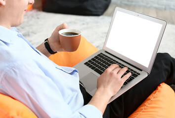 Wall Mural - Young man drinking coffee while using laptop in office