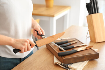 Woman sharpening knife in kitchen, closeup