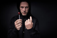 Terrible Threatening Adult Man In Black Wear Offering Candy Lollipop To Children Standing On Black Studio Background, Portrait Of Caucasian Maniac Pedophile Male Looking At Camera Confidently