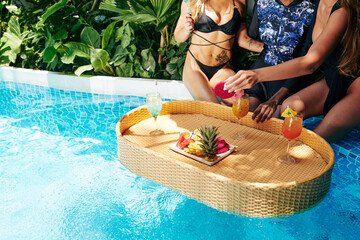 Wall Mural - Group of young women enjoying fresh fruits and sweet delicious cocktails when enjoying hen pool party