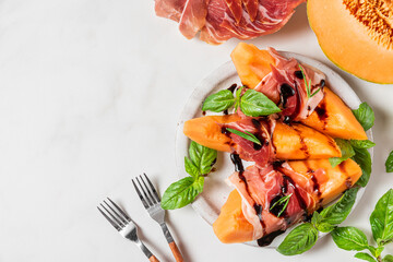 Wall Mural - Prosciutto ham with melon cantaloupe slices, balsamic vinegar sauce and basil in a plate on white background. top view