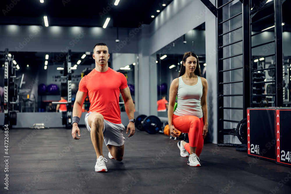 A cute sports couple exercising steps forward for legs and buttocks on a black floor in an indoor gym with a mirror. Fitness and sports lifestyle - obrazy, fototapety, plakaty 