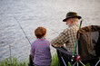 Caucasian senior fisherman teaching cute grandkids fishing on lake in nature, casually dressed. Elderly male help child boy, support and talk. Outdoor portrait, copy space