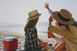 © ViDi Studio - Back rear view friends young women in straw hat summer clothes have picnic hang out together drink liguor hold glasses cover with hands outdoor on sea beach background People vacation journey concept.