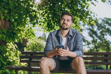 Wall Mural - Bottom view minded young man in blue shirt sitting on wooden bench use mobile cell phone chat online rest relax in spring green city park sunshine outdoors on nature Urban lifestyle leisure concept