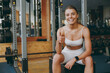 © ViDi Studio - Young smiling resting strong sporty athletic sportswoman woman 20s wear white sportswear warm up training sitting near treadmill trainers show thumb up in gym indoors Workout sport motivation concept