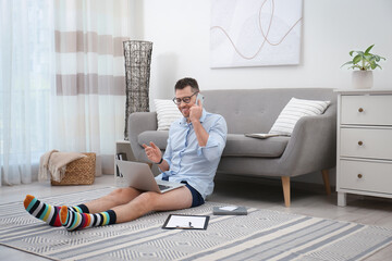 Wall Mural - Businessman in shirt and underwear talking on phone during video call at home