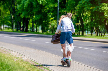 A guy and a girl rides an electric scooter in the summer Park
