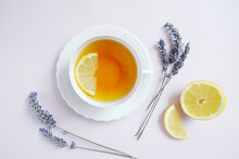 White Teacup Of Tea With Lemon, Dry Lavender On The Light Purple Background. Composition In Harmony And Balance. Minimal Summer Fall Concept. Flat Lay. French Style. Tea Lovers Boutique.