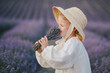 Cute little girl wearing white dress and straw hat holding bunch of flowers in a lavender field.