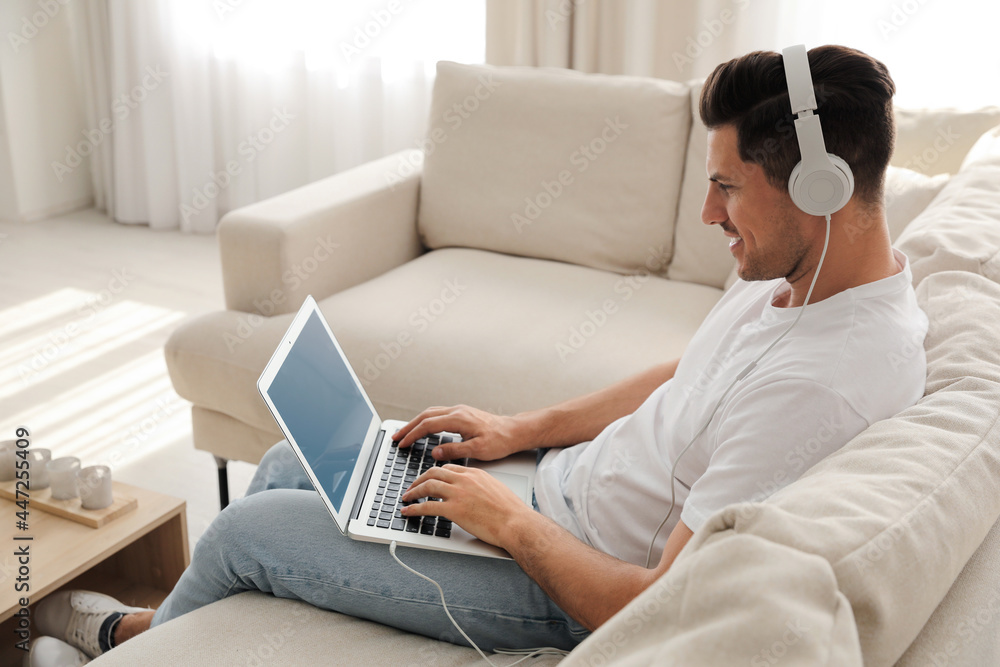 Man with laptop and headphones sitting on sofa at home - obrazy, fototapety, plakaty 