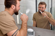 © Roman - Healthy male in casual outfit brushing teeth. Electric toothbrush used by handsomr guy, in bathroom. healthcare morning procedures concept. copy space. people lifestyle, modern devices, smart house