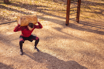 Wall Mural - Muscular man doing squats with tree log outdoors