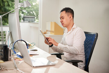 Wall Mural - young software engineer sitting at office desk and testing new application he was working on on tabl