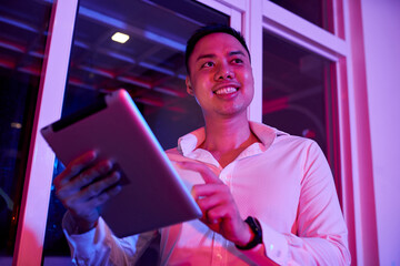 Happy young businessman working on tablet computer in dark office with led light