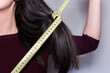 © AliciaFdez - Detalle de una mujer sosteniendo una cinta métrica amarilla alrededor de un mechón de su cabello largo. Primer plano de una cinta de medir con números que se muestran.