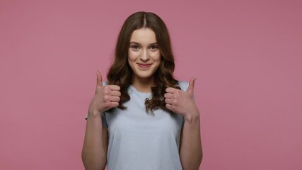 Wall Mural - Young pretty woman wearing casual style T-shirt expressing happiness, showing thumbs up to camera, enjoying good news, celebrating. Indoor studio shot isolated over pink background.