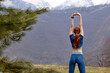 Rear view on redhead fitness woman stretching arms before workout training in nature, magnificent mountains landscape in the background. view from back on slim athlete female training, exercising