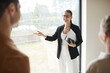 © Seventyfour - Minimal waist up portrait of smiling real estate agent giving apartment tour to couple while standing by window, copy space