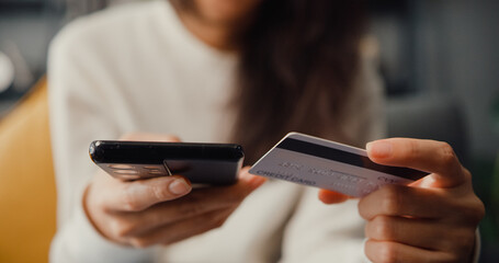 Closeup young asia lady use cellphone order online shopping product and paying bill with credit card sit on couch in living room at house, Quarantine activity, Fun activity for coronavirus prevention.