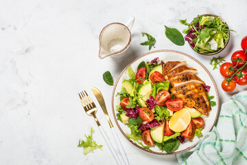 Healthy salad with Grilled chicken fillet, fresh leaves, avocado and vegetables. Top view at white marble table.