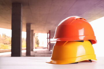 Hard hats on white wooden surface at construction site with unfinished building. Space for text