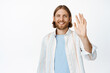 © Cookie Studio - Portrait of friendly bearded guy, ordinary man with blond hair smiling happy, waving hand, say hello, hi gesture, greeting friend, standing over white background