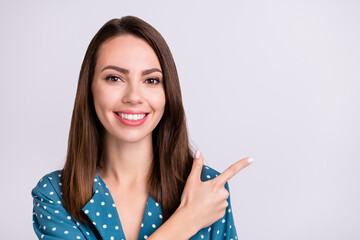 Poster - Photo of sweet shiny young lady wear dotted shirt pointing finger empty space smiling isolated grey color background