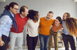Multiracial diverse business team hugging looking at each other with friendly smile during work break. Group of people in modern office hall giving support at business training or therapy session