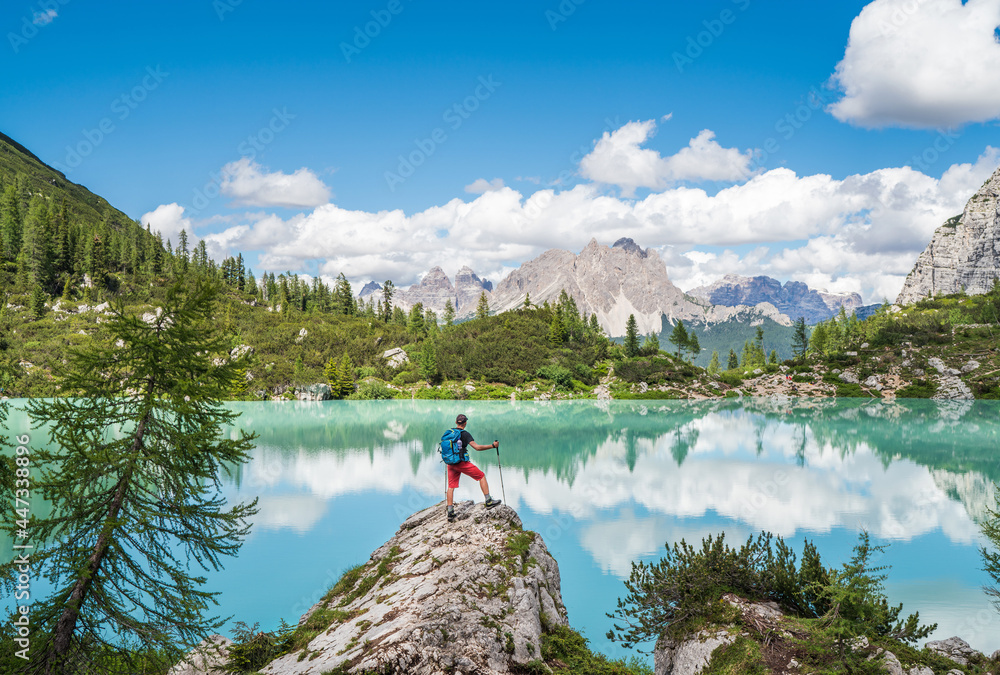 Backpacker with backpack enjoying the turquoise Lago di Sorapiss 1,925m altitude (mountain lake) view as he has mountain walk in Dolomite Mountains, Italy. Active people in nature concept. - obrazy, fototapety, plakaty 