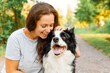 © Юлия Завалишина - Smiling young attractive woman playing with cute puppy dog border collie on summer outdoor background. Girl holding embracing hugging dog friend. Pet care and animals concept