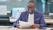 © stockbakers - Young African Businessman Celebrating Success While Reading Documents