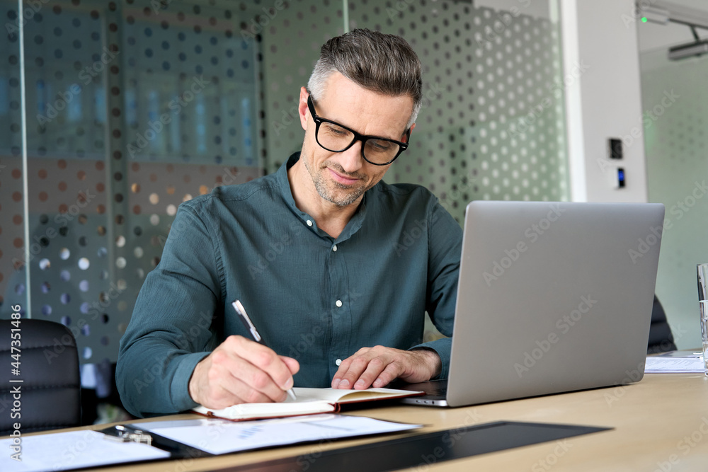 Happy mature executive ceo manager using laptop writing notes in notebook at workplace. Smiling middle aged business man working in office analyzing financial data doing research. Stock Photo | Adobe Stock