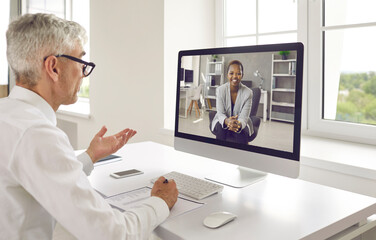 Two happy business people discussing work in virtual online meeting. Senior male executive manager or recruiter talking to new young female colleague or job seeker via video call on modern computer