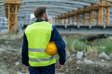 Poster - Rear view of builder in reflective clothing standing on construction site and working