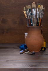 Sticker - Paint brush in clay jug and used tubes on wooden table background . Paintbrush for art painting