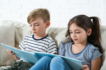 Canvas Print - Little boy and girl reading book on sofa at home