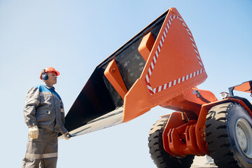 Professional mechanic in hard hat holds on to lifting mechanism of bulldozer bucket for loading coal