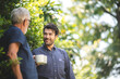 © chokniti - adult son and elderly senior father talking together and holding coffee cup in the garden, happy morning lifestyle of man generation family, love day at home