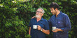 © chokniti - adult son and elderly senior father talking together and holding coffee cup in the garden, happy morning lifestyle of man generation family, love day at home